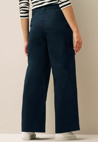 Navy cargobroek met wijde pijpen, gemaakt van zachte stof. Kenmerken zijn zijzakken, riemlussen en een gepaste tailleband. Gepaard met witte sneakers.