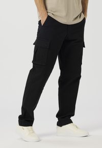 Sorte cargobukser laget av bomull, med sidelommer i lappestil og rett bein, kombinert med hvite joggesko.