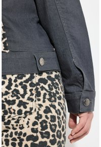 Jeansjack in donkergrijs met een gestructureerde afwerking, met een luipaardprintpatroon op de broek. Knopen accenten detailleren het jack.