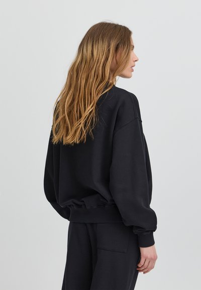 Felpa nera oversize con vestibilità rilassata, polsini e orlo a coste. Caratterizzata da un tessuto morbido e un design minimalista.