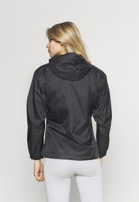 Chaqueta ligera negra con capucha, con puños elásticos y dobladillo ajustable. Textura suave y diseño minimalista.