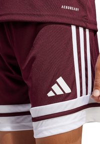 Bordeauxfarbene Sportshorts aus glattem Material mit weißen Akzenten, ausgestattet mit drei vertikalen Streifen und dem Adidas-Logo in Weiß.