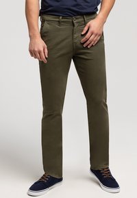 Oliwkowe chinosy o wąskim kroju, z zapięciem na guzik i przednimi kieszeniami, w połączeniu z granatowymi butami i ciemnoniebieską koszulą.