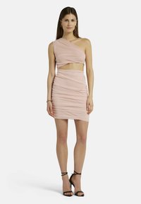 Rosa, einseitiges Kleid mit geraffter Textur, Ausschnitt in der Taille und Mini-Länge. Kombiniert mit schwarzen, geschnürten High Heels.