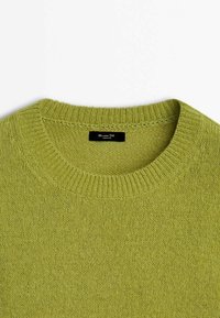 Pull vert clair en maille avec col rond côtelé et une petite étiquette noire à l'intérieur de l'encolure.