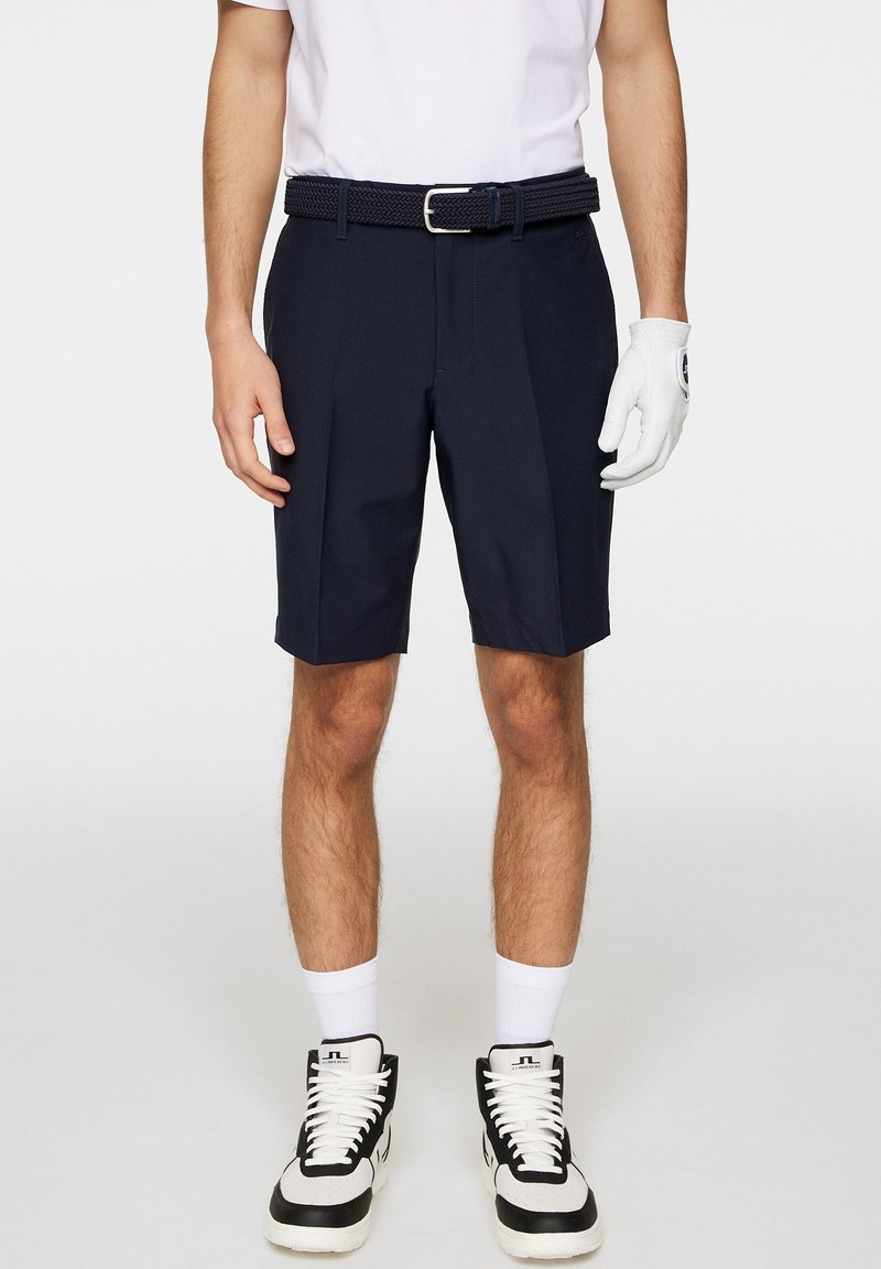 Mörkblå shorts med skräddarsydd passform, prydda med ett texturerat flätat bälte, i kombination med vita sportstrumpor och svartvita träningsskor.