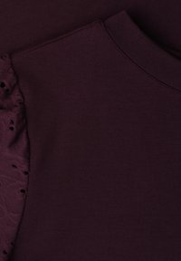 Tissu tricoté violet foncé avec col roulé côtelé et détail en dentelle volantée sur la partie supérieure gauche de la manche.