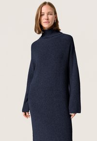Dreptunghiul bleu marin din tricot, cu gât înalt, mâneci lungi și o croială lejeră, evidențiind un material texturat de greutate medie.