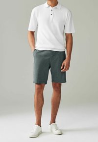 Polo shirt blanc avec trois boutons noirs, associé à un short gris et des baskets blanches. Coupe standard avec des manches courtes et des poches latérales.