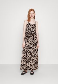 Rochie maxi din țesătură cu imprimeu leopard, cu bretele fine, având o talie strânsă și o textură ușoară. Pantofii negri cu talpă joasă completează ținuta.