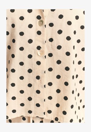 Paido-paita vaaleasta beige-kankaasta, jossa on mustia pilkkuja. Varustettu pyöreillä nappeilla ja hieman teksturoidulla pinnalla.