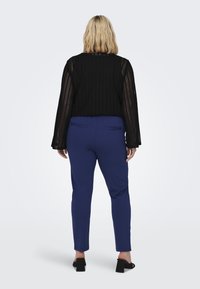 Černý svetr s otevřeným pletením a zvonovými rukávy, zkombinovaný s utaženými modrými kalhotami. Outfit má ležérní siluetu a hladkou texturu látky.