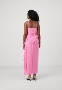 Maxi dress in soft pink chiffon with thin straps, featuring a draped layer at the back and ruffled accents along the hem.