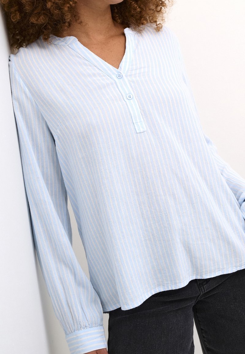 Chemise à manches longues à rayures bleu clair avec col en V, dotée d'une patte de boutonnage et d'un ourlet légèrement courbé. Tissu doux, coupe décontractée.