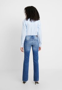 Lyseblå stribet skjorte stoppet ned i medium-blå flared jeans med let fading. Mørkeblå hælstøvler er synlige forneden.