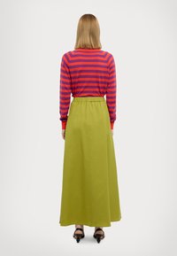 Gonna lunga e verde con cintura elastica, abbinata a una maglia a maniche lunghe a righe rosse e viola. Il tessuto appare liscio e leggero.