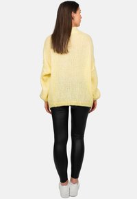 Pull en tricot surdimensionné en jaune pastel avec des poignets côtelés. Assorti à des leggings en simili cuir noir et des baskets blanches.