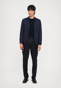 Navy blazer paired with a black sweater and tailored black trousers, finished with black leather shoes. Slim-fit design with clean lines.