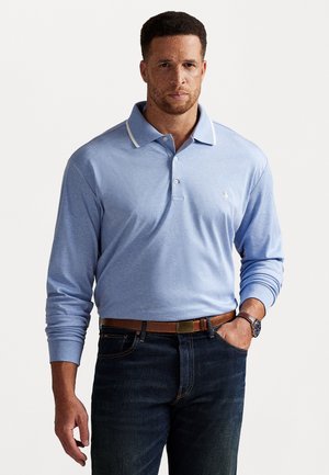 Langermet polo i lyseblått stoff med hvit kragestripe, treknappet placket og lite logo. Kombinert med mørk denim jeans og et brunt belte.