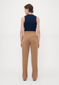 Navy mouwloos topje gecombineerd met tan hoge taille broeken met een soepele textuur en een detail van een achterzak, gezien van achteren.