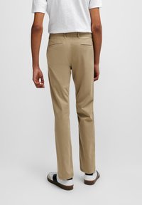 Pantalon beige à coupe droite, doté de deux poches arrière et d'un tissu lisse. Stylé avec une chemise blanche et des baskets blanches avec des accents noirs.