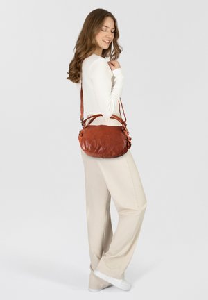 Bruine leren crossbody tas met een zachte textuur, ronde vorm, verstelbare schouderband en decoratieve hardware-details.
