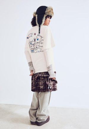 Tricou crem cu imprimeu grafic, purtat sub o fustă scurtă cu carouri maro. Pantaloni gri din catifea și o pălărie neagră cu blană la margine completează ținuta.