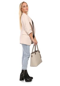 Lichtbeige blazer met opgerolde mouwen, zwarte top, lichtblauwe jeans en zwarte enkellaarzen met hak. Draagt een gestructureerde lichtgrijze handtas.