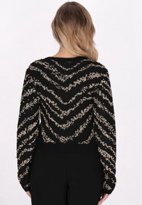 Maglione a strisce nere e oro con un motivo a zigzag, orlo a coste e dettagli in perline dorate sulle maniche. Texture a maglia morbida.