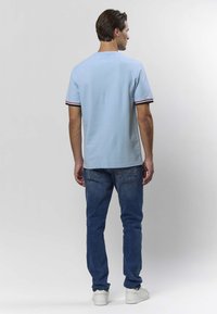 Ljusblå kortärmad pikétröja med svart- och rödrandiga muddar, kombinerad med blå jeans och vita sneakers; slät tyg, avslappnad passform.