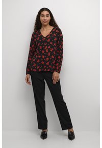 Zwarte lange mouw top met rood bloemenpatroon, V-hals; gecombineerd met zwarte broek en zwarte platte schoenen. Getextureerde stof, relaxte pasvorm.