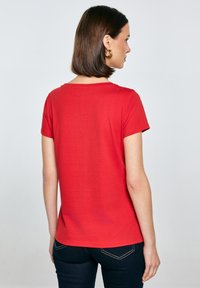 Červené bavlněné tričko s krátkými rukávy, kulatým výstřihem a přiléhavým střihem. Hladká textura, bez vzorů nebo zdobení. Jednoduchý design.