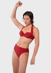 Červený bikiny set, ktorý obsahuje top bez ramienok s podšívkou a dekoratívnym švom, a vysoké spodky s riasením po stranách. Hladká textúra látky.