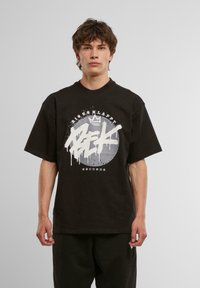 Sort oversized t-shirt lavet af bomuld, med et hvidt grafisk print med splattereffekt og teksten "BIS SKLAPR RECORDS" arrangeret cirkulært.