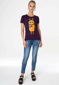 Purple t-shirt featuring a cartoon character with orange body and brown accents. Paired with blue skinny jeans and black platform shoes.