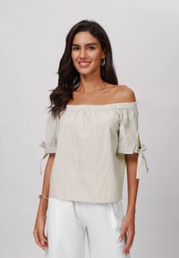 Gestreiftes Crop-Top mit schulterfreier Silhouette in Hellgelb und Weiß, mit kurzen Ärmeln, die an den Bündchen gebunden sind. Glatter Stoff und lockere Passform.