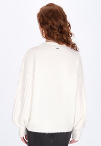 Witte, oversized trui met geribde mouwen en achterkant, zachte textuur, ronde hals en een klein labeldetail bij de halslijn.