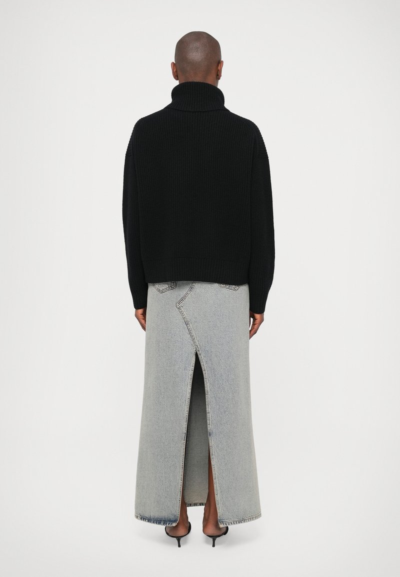 Svart ribbad polokrage tröja, i kombination med en lång grå denimkjol med hög slits och kontrasterande sömnadsdetaljer.