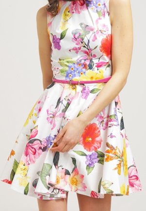 Robe blanche sans manches avec de grands motifs floraux colorés et une fine ceinture rose autour de la taille.