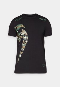 T-shirt en coton noir avec un grand graphique camouflage et le texte "Venum" en vert sur les épaules. Manches courtes, coupe standard.