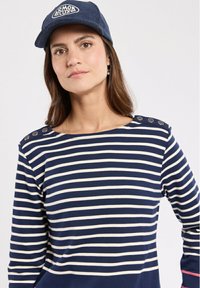 Top a maniche lunghe a righe blu navy e crema con bottoni decorativi sulla spalla. Abbinato a un cappellino in velluto a coste blu navy con logo.