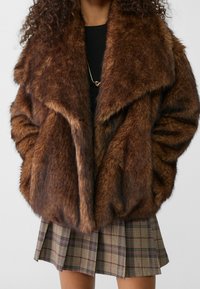 Bruine faux fur jas met een grote kraag, met een dikke textuur en een losse pasvorm. Gecombineerd met een geruiten rok.
