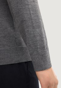 Gray knit sweater sleeve with ribbed hem, smooth texture, and fitted shape. Subtle variation in knit pattern.