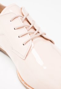 Chaussure habillée en cuir rose pâle brillant avec des lacets assortis et des coutures détaillées sur une semelle en bois.
