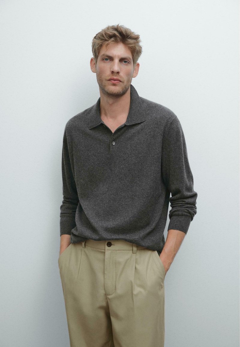Graphitgraues Strick-Polo-Shirt mit weicher Textur, langen Ärmeln und Kragen, kombiniert mit hochgeschnittenen beigen Hose und einem Knopfdetail.