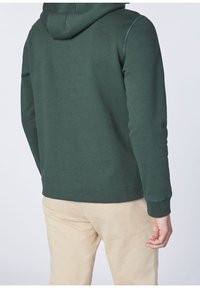 Felpa verde in cotone con cappuccio regolabile e cuciture laterali, dotata di polsini e orlo a coste. Presenta una texture liscia.