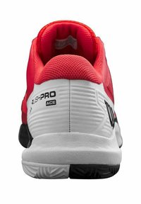 Zapatilla de tenis roja y blanca con parte superior texturizada, cuello acolchado y talón moldeado. Presenta la marca "RUSHPRO ACE" en el lateral. Suela negra.