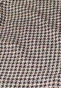 Tejido de punto que presenta un patrón de pata de gallo en negro, blanco y durazno, con una superficie texturizada, adecuado para diversas aplicaciones textil.