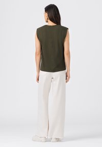 Olivgrön ärmlös topp med rak skärning, med en liten dragkedja i ryggen. Kombinerad med vida vita byxor och vita sneakers.