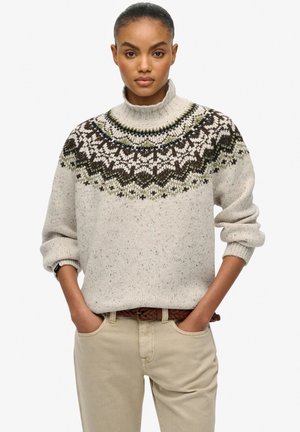 Pullover di maglina beige chiaro con collo alto, caratterizzato da un giogo decorato in marrone scuro, verde e bianco. Tessuto a trama continua con punteggiature.